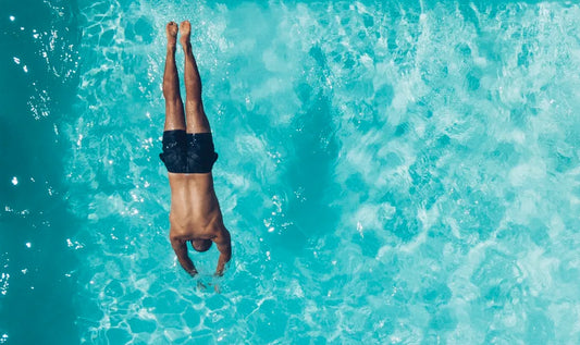 Ein Mann springt in türkis-klares Wasser eines Pools - symbolisch für das frische Tragegefühl von Viskose-Herrenunterwäsche an heißen Sommertagen